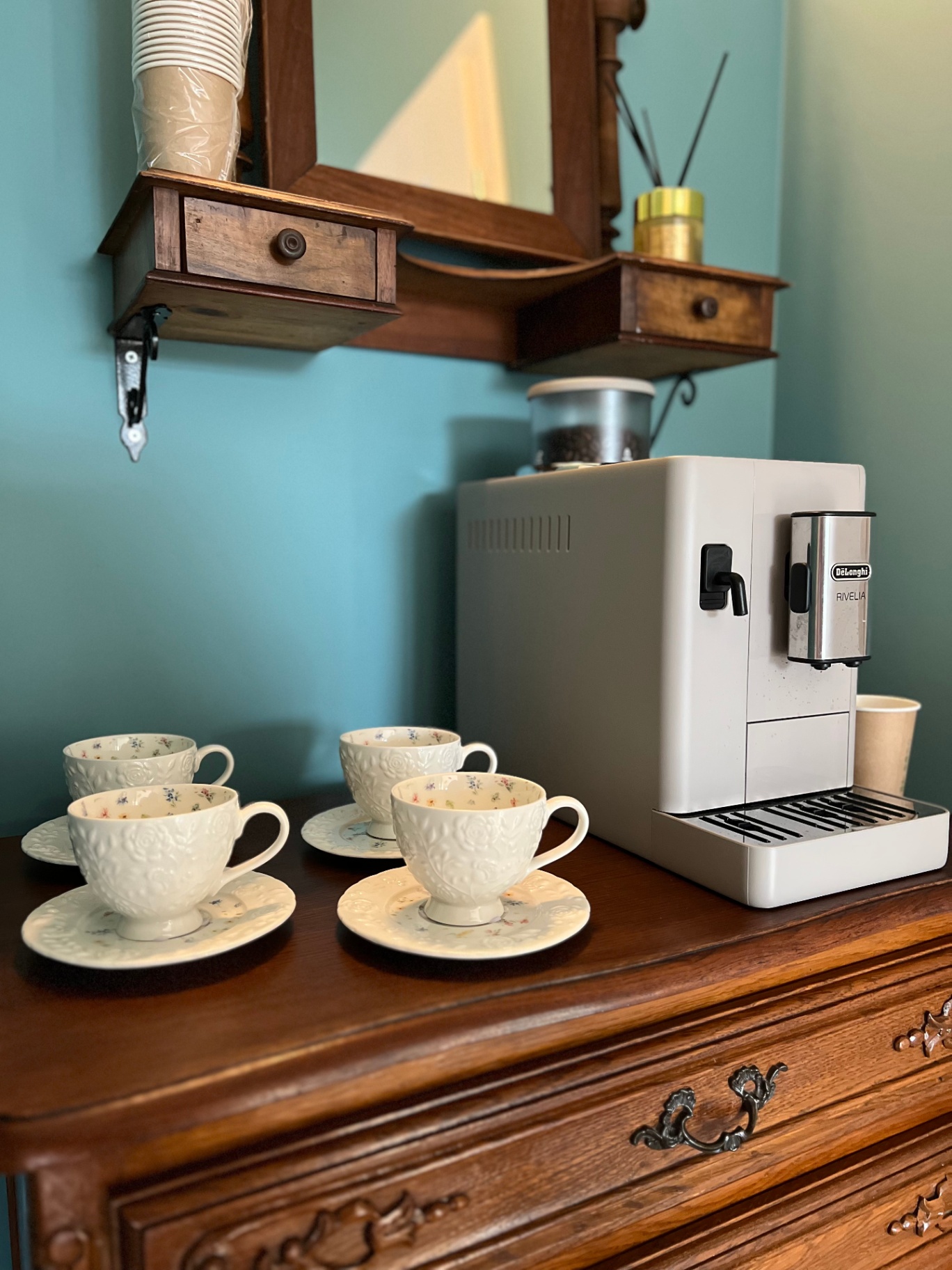 Porcelanowe filiżanki i ekspres ciśnieniowy na zabytkowej komodzie